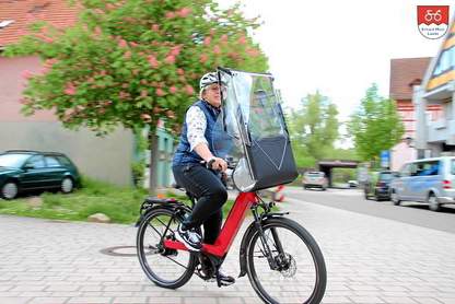 E-Bike für Hausmeisterservice und Alltagswege Frau mit E-Bike und Wetterschutz bei einer Fahrt im Alltag oder Hausmeisterservice